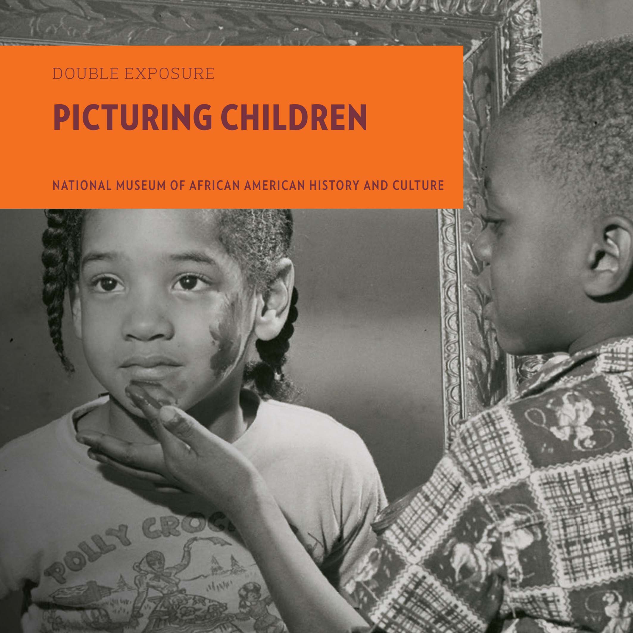 Black and white photograph with a young boy applying face paint to the chin of a young girl using his left finger. The top right portion of a large mirror with ornate framing is behind the girl.