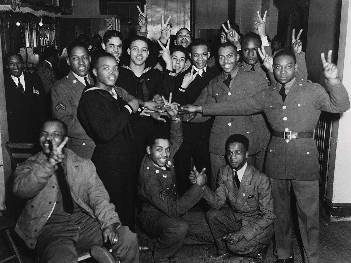 Servicemembers in a group with their hands held up with a "V" sign.