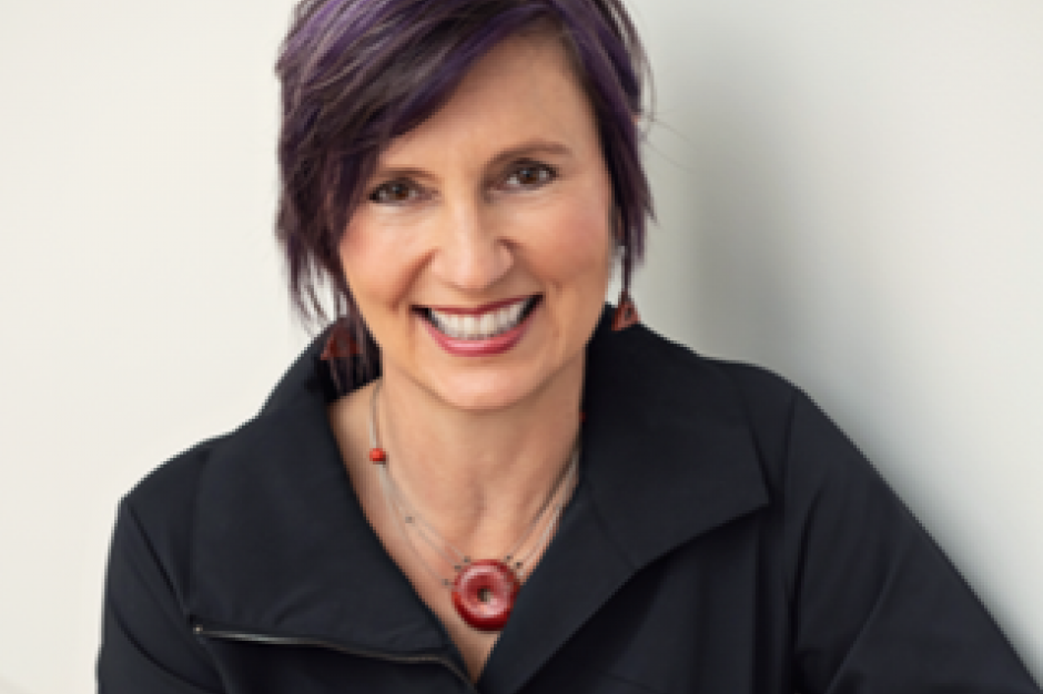portrait photo of a smiling woman with purple and black hair, wearing a black top and neckless with a red disc.
