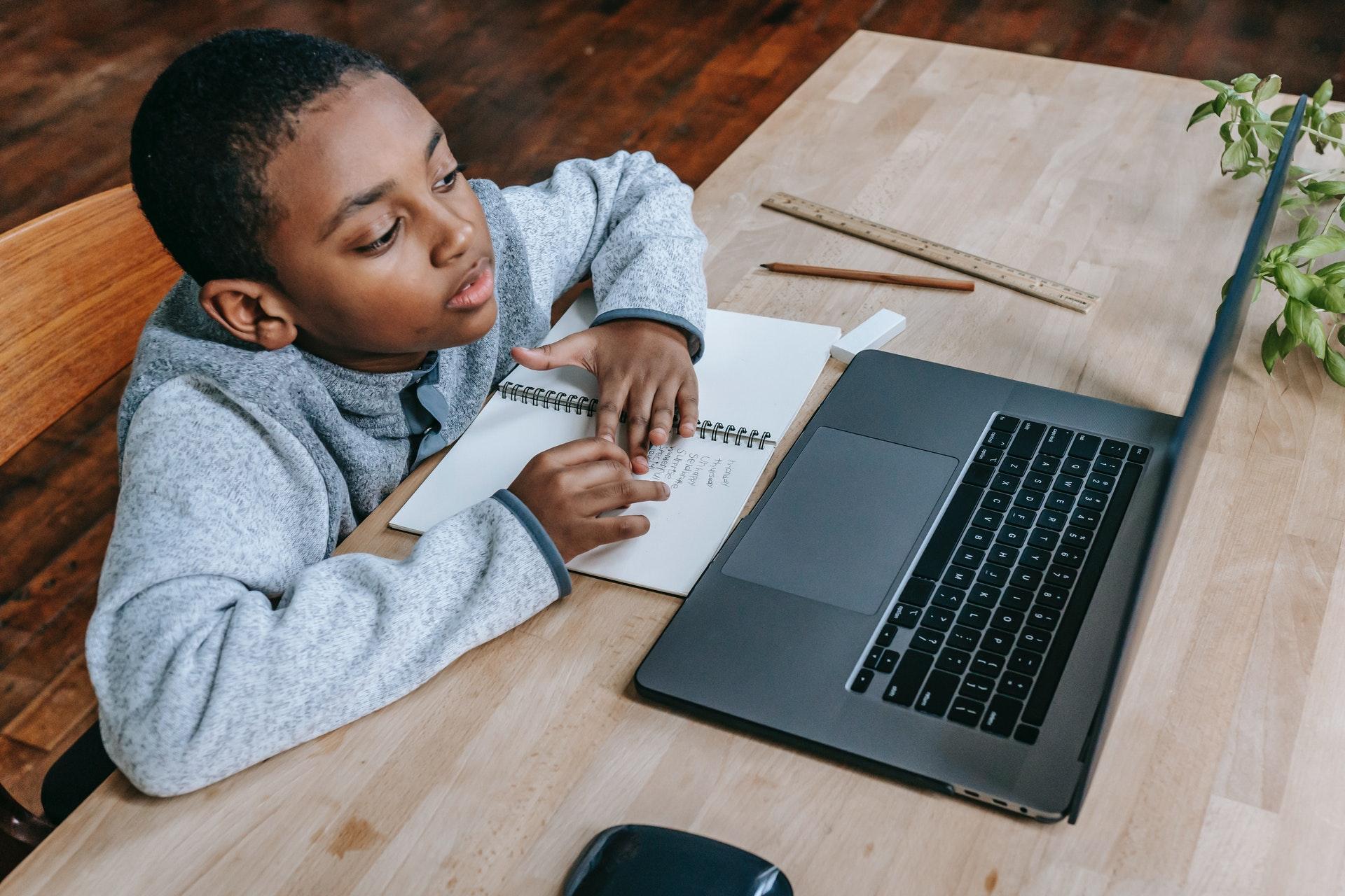 young African American boy sitting at a desk in front of a laptop computer