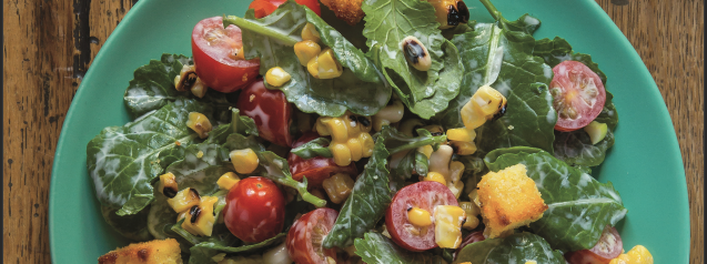 Baby Kale Salad pictured on plate. Wooden table in background .