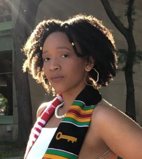 Image of a woman wearing a white blouse and pearl necklace. She has a Kente cloth patterned scarf draped over her shoulders