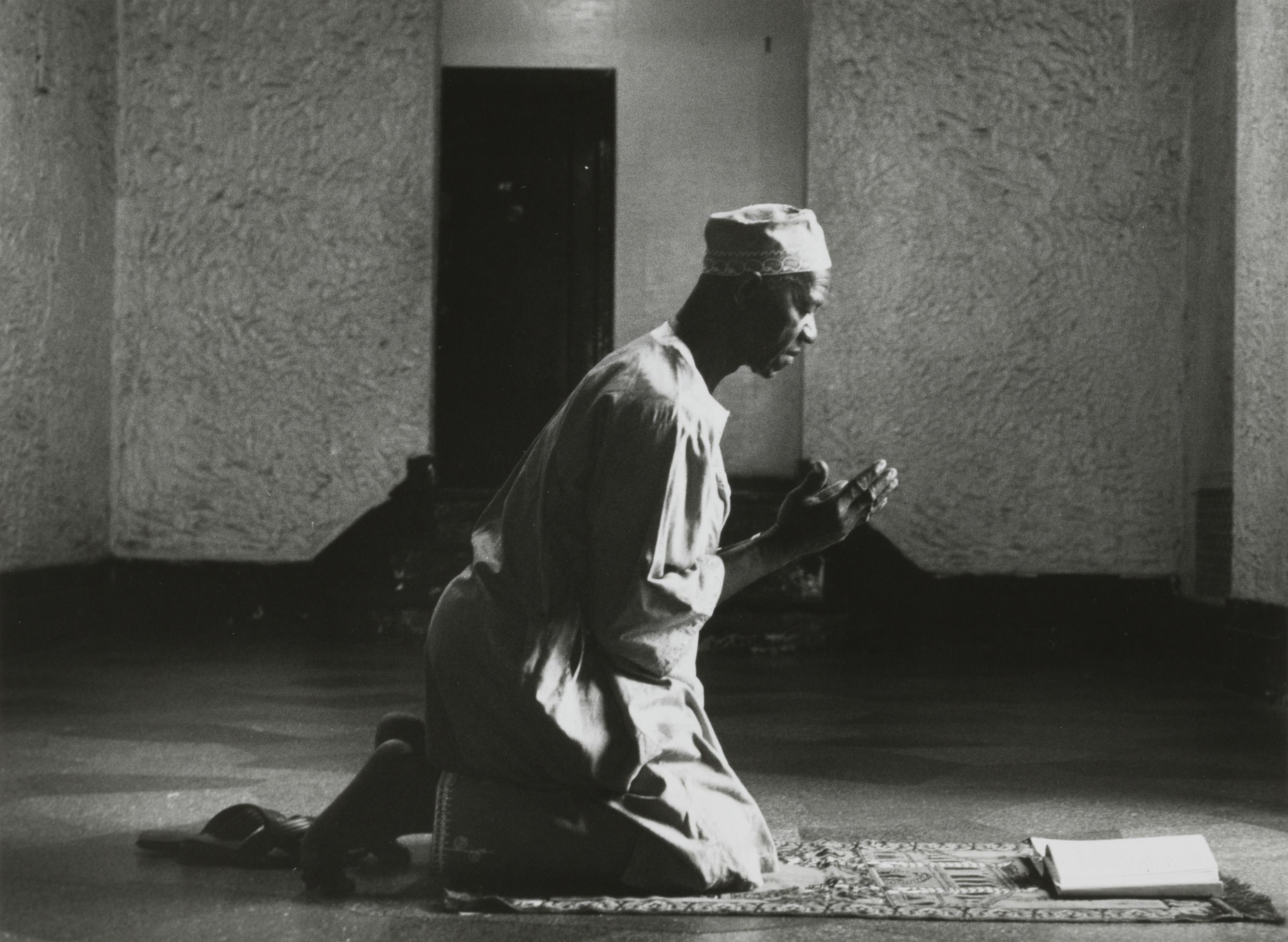 A man kneeling on a rug in prayer.