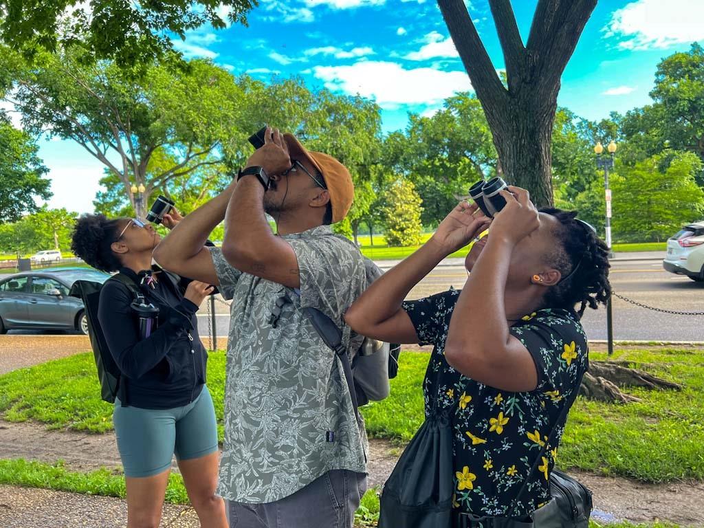 Image of an African American man and African American women using binoculars to find birds in trees