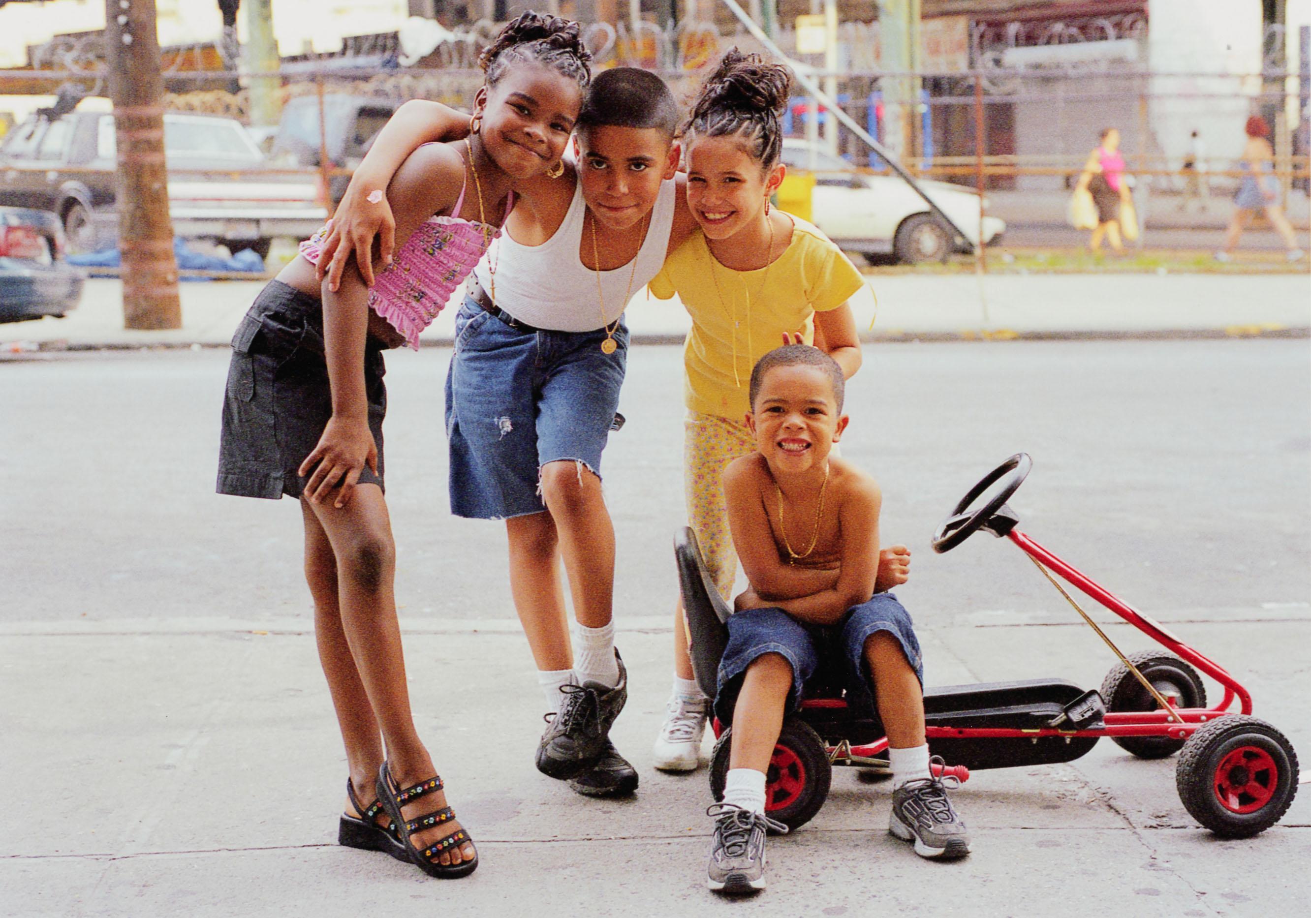The photograph depicts a full-length image of four children posed on a sidewalk.