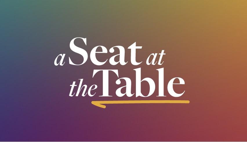 A logo with text that reads "A Seat at the Table"