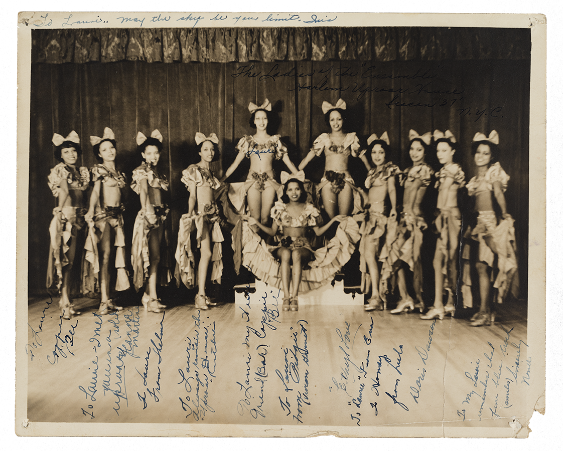 a black-and-white image of a group of eleven (11) women wearing matching costumes and posing on stage.