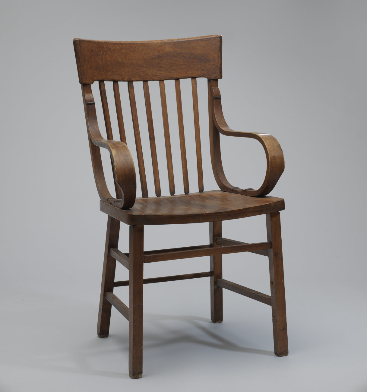 The chair has curved arm rests. The arm rests are attached to the chair back and seat with oval-shaped, metal cleats.