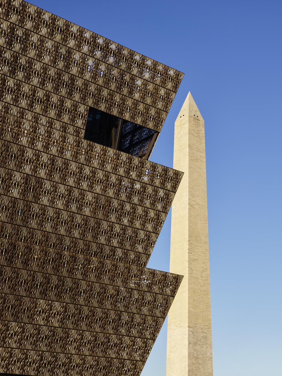 View of the NW corner of the NMAAHC building with Washington Monument in the background.