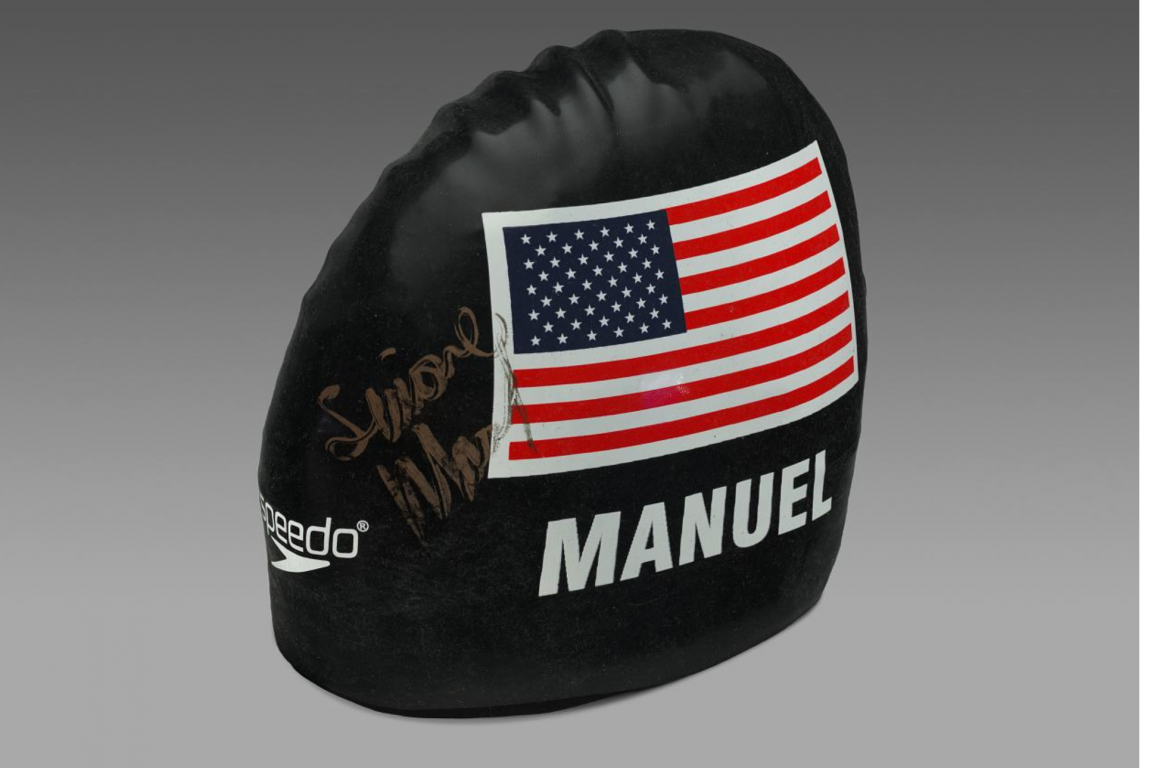 Swim cap worn and signed by Simone Manuel at the 2016 Olympics in Rio.Cap is signed in gold text. navy blue cap with an image of US flag and MANUEL written on it..