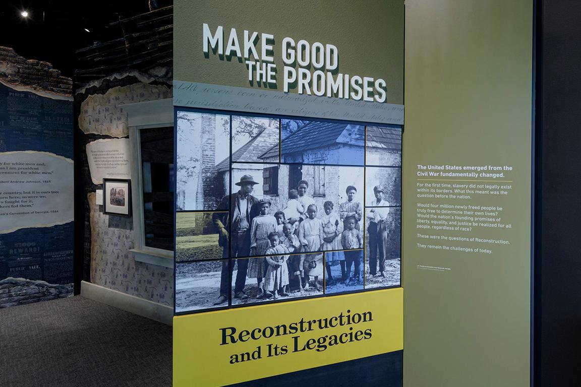 Make Good the Promises Exhibition opening. Sign that says "Reconstruction and Its Legacies" in black in with yellow background. An African American family is pictured above