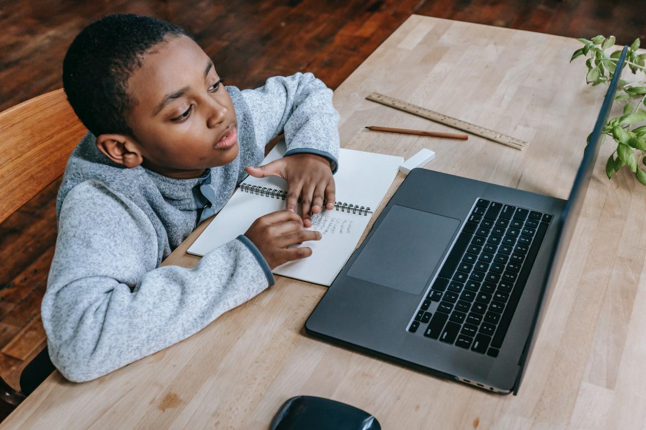 young African American boy sitting at a desk in front of a laptop computer