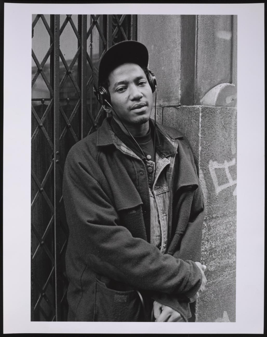 Black and white photo of a man standing against a concrete wall on a city street
