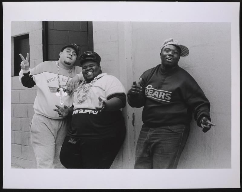 Black and white image of three rappers posed against a wall in 80's gear