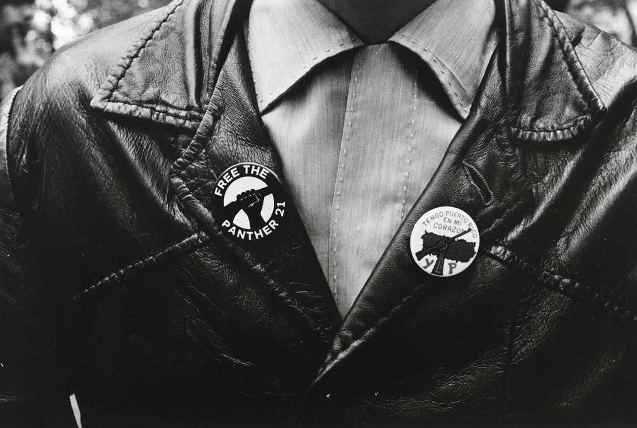 A black and white photograph of an unidentified person wearing a leather jacket and two buttons.