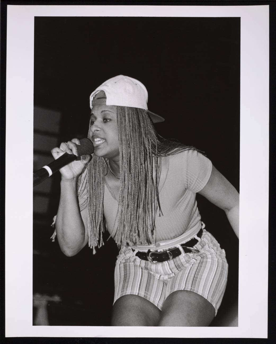 Black and white image of a woman with a backward hat rapping int a microphone