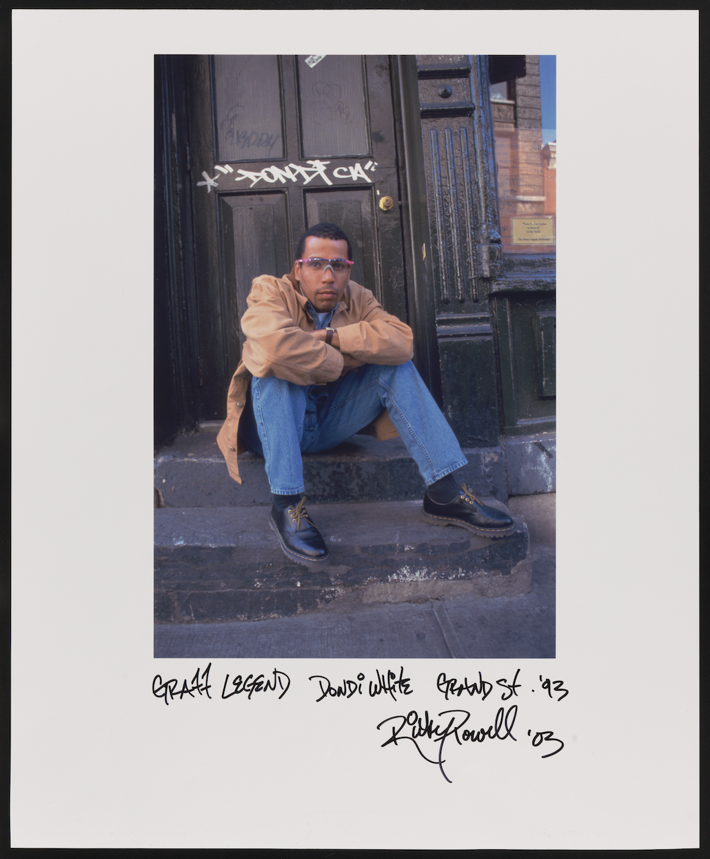 A man sitting on city steps with graffiti on the door behind him