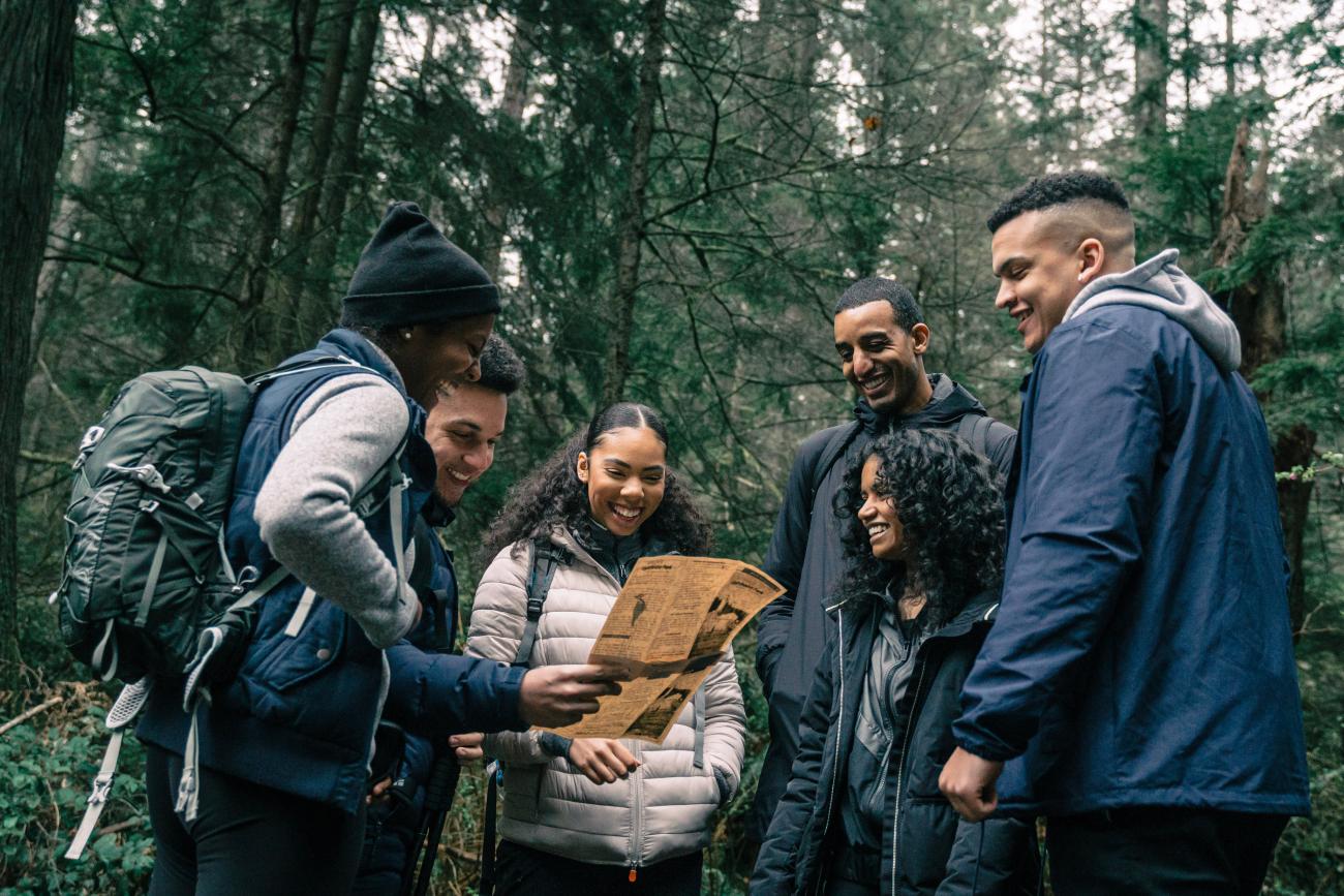 A diverse group of people standing in the woods on a hike and reading a map.