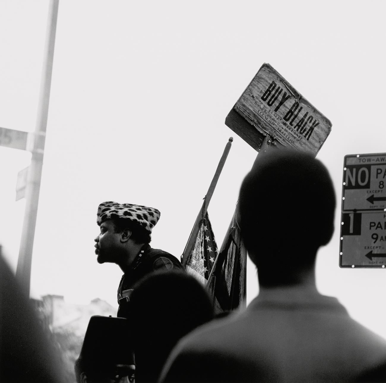 The photograph depicts Charles Peaker, the head of the African Nationalist Pioneer Movement (ANPM), standing on the corner of 125th Street, above a crowd of people.
