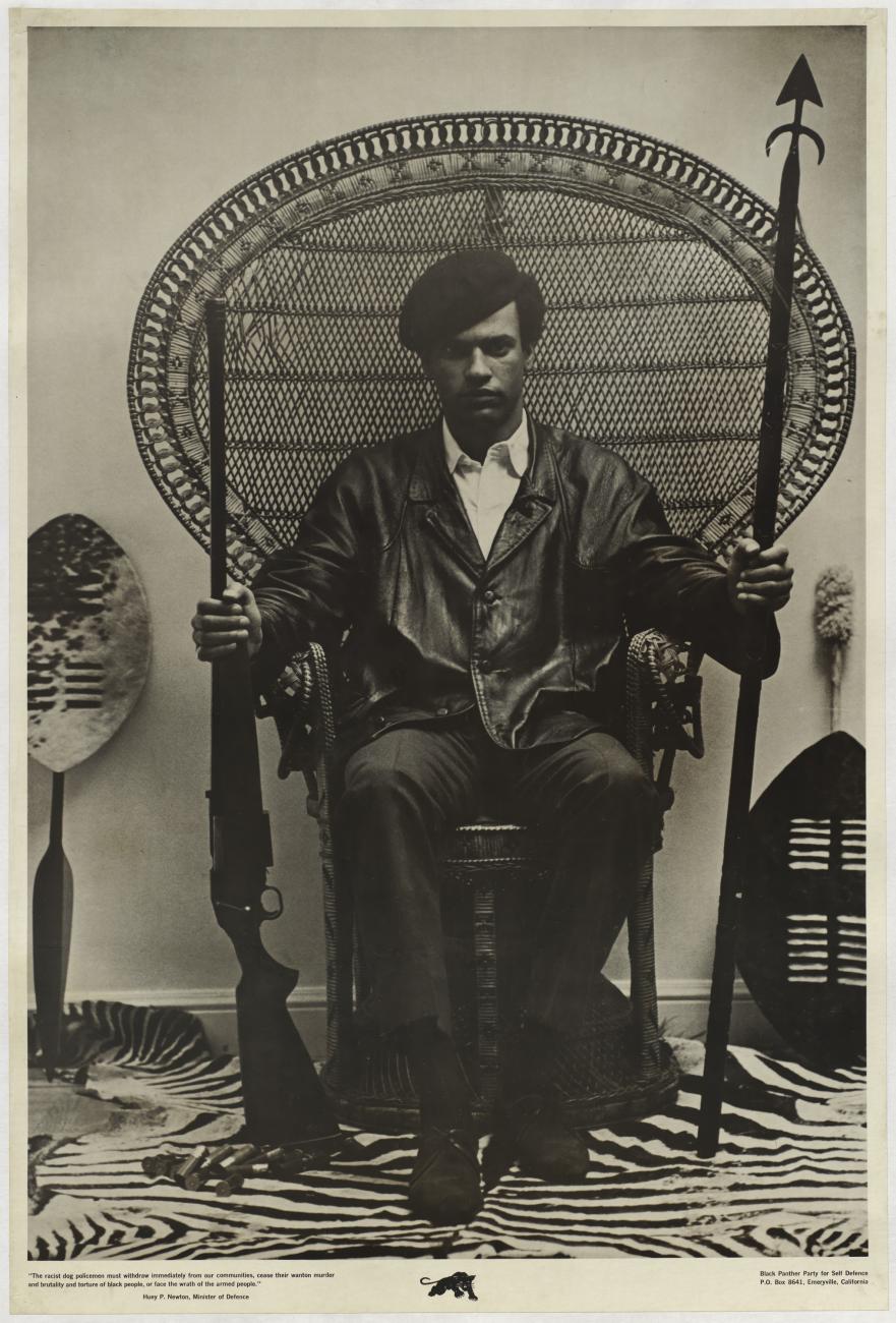 Poster of Huey Newton sitting in a chair holding a rifle. 