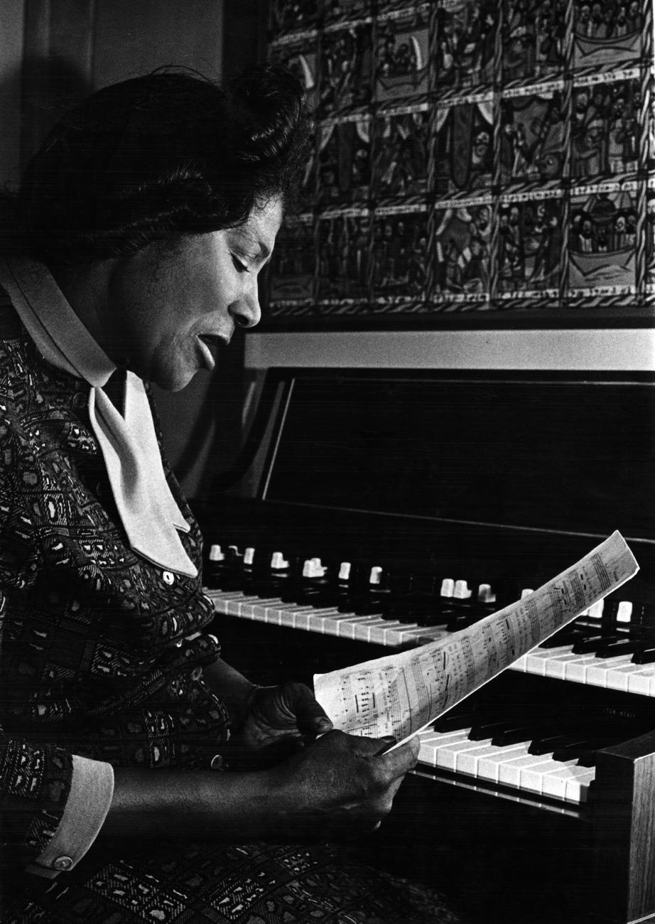 Image of Mahalia Jackson seated at an organ. She is hold ing sheet music.