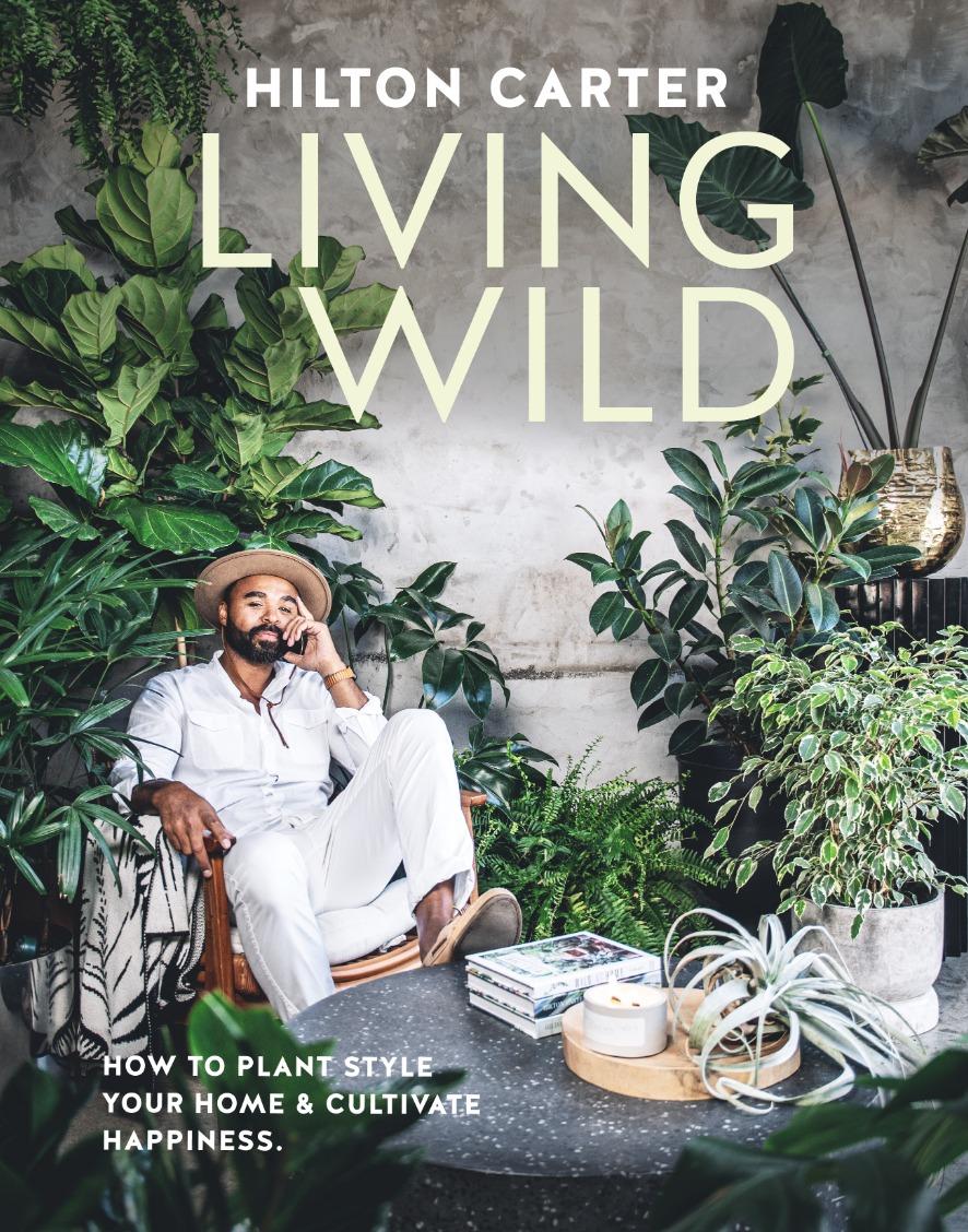 COver of Hilton Carter's "Living Wild". Hilton is pictured sitting at a table with one foot up and is surrounded by plants