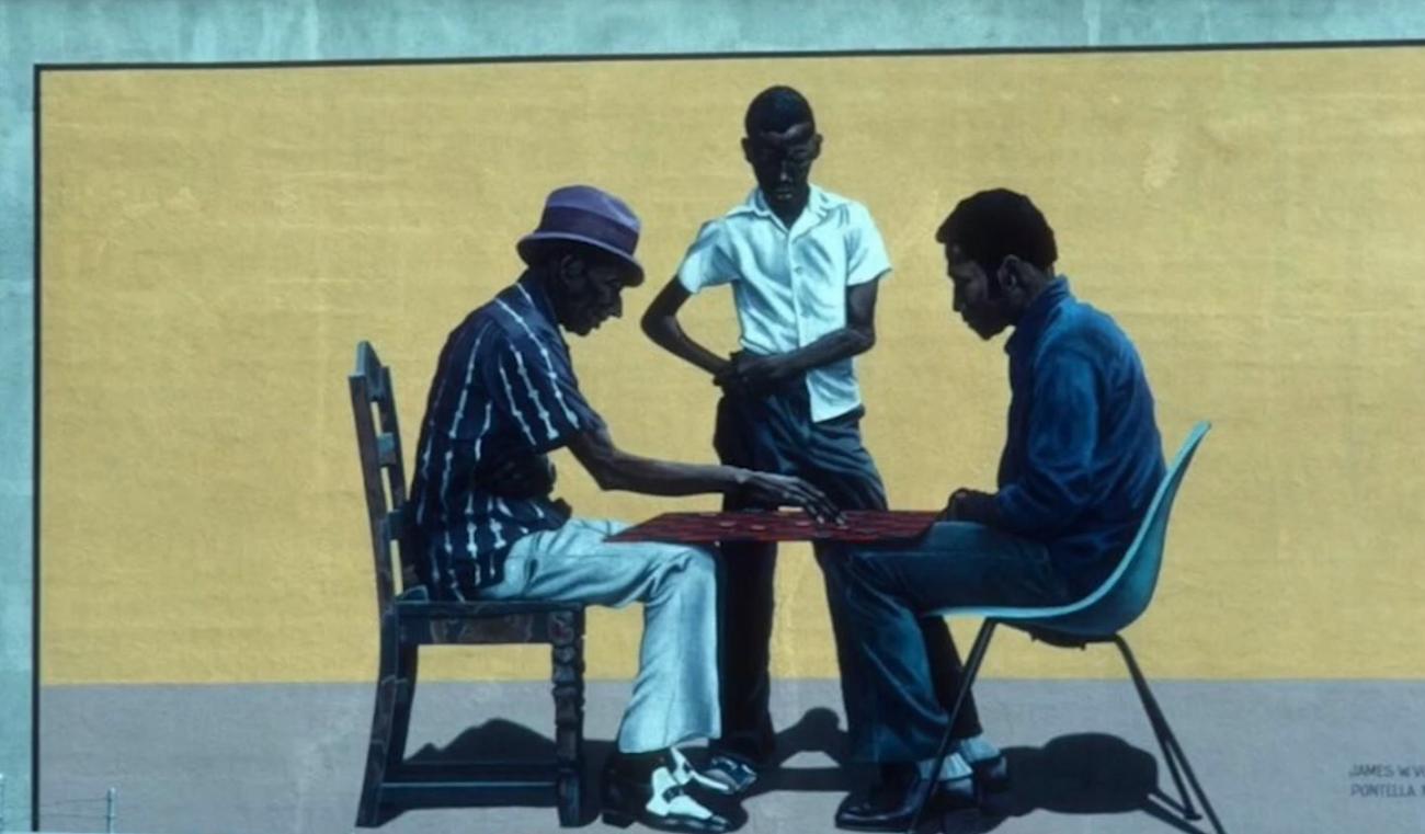 A portion of a mural depicting two men seated across from eachother with a younger man standing between them