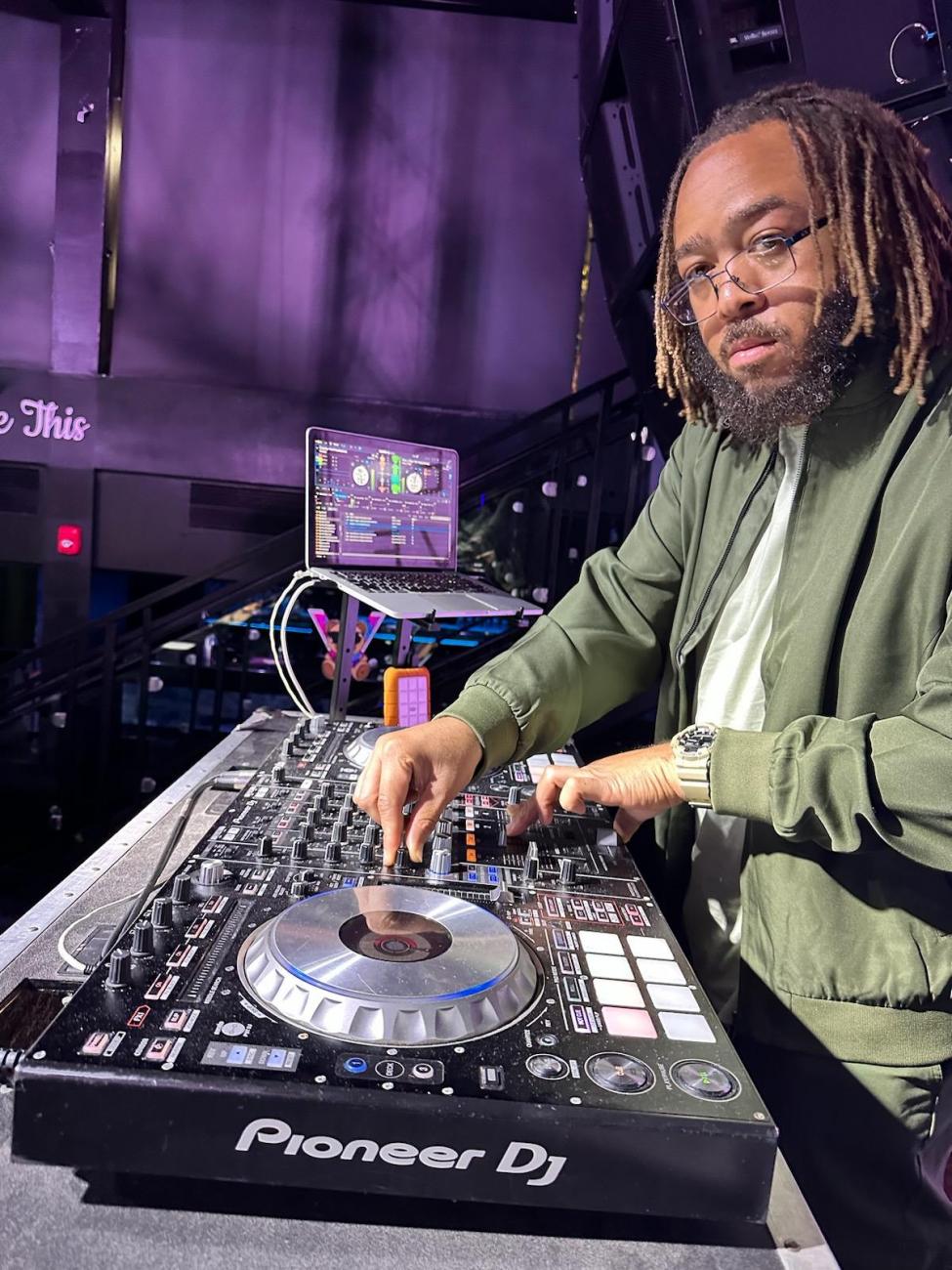 Headshot of DJ Reddz at a table table spinning records, smiling into camera