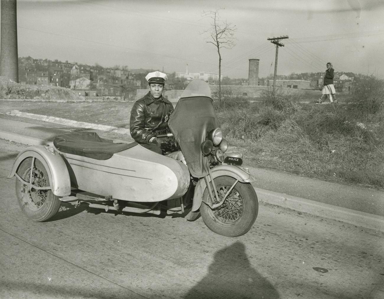 A black and white photograph of a policeman sitting in a motorcycle with a sidecar.