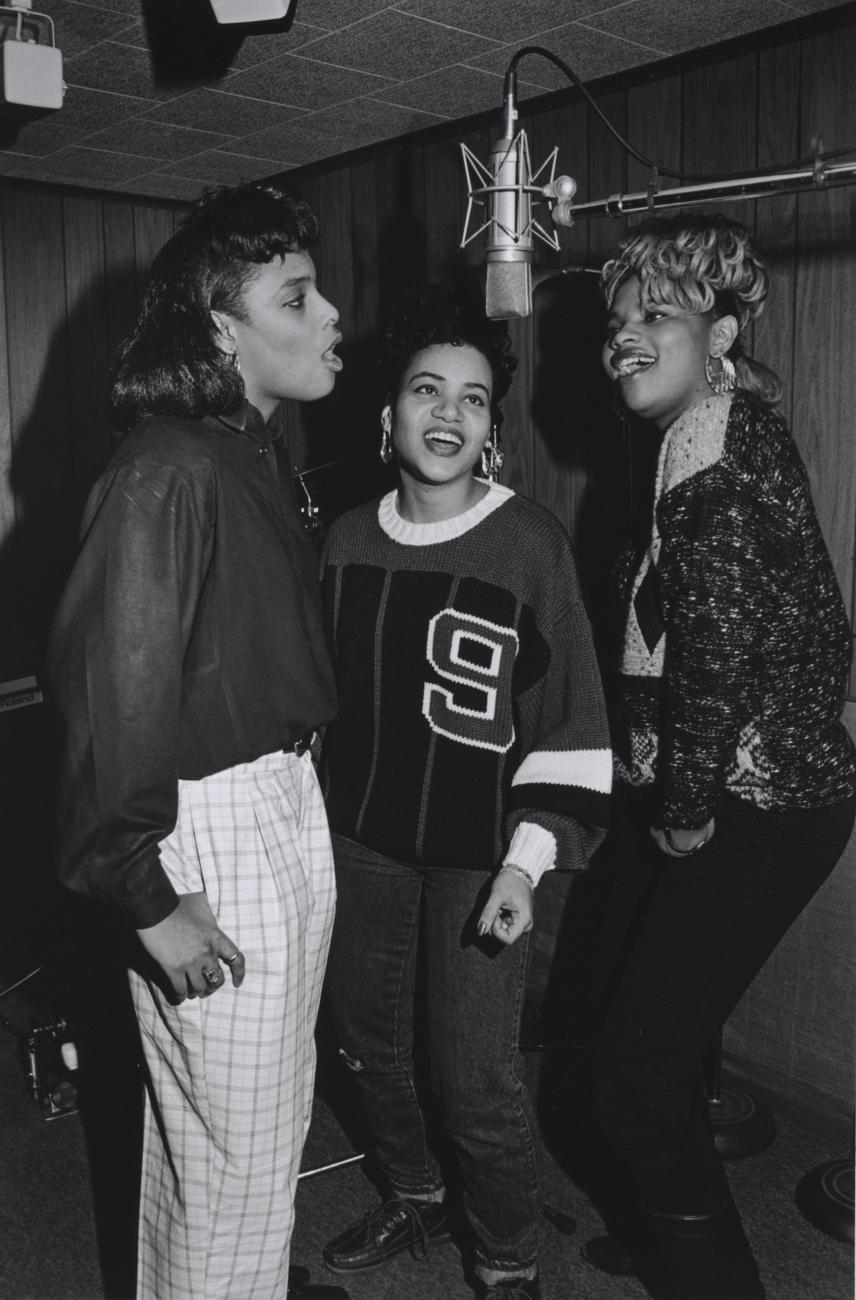 Three women around a microphone. 