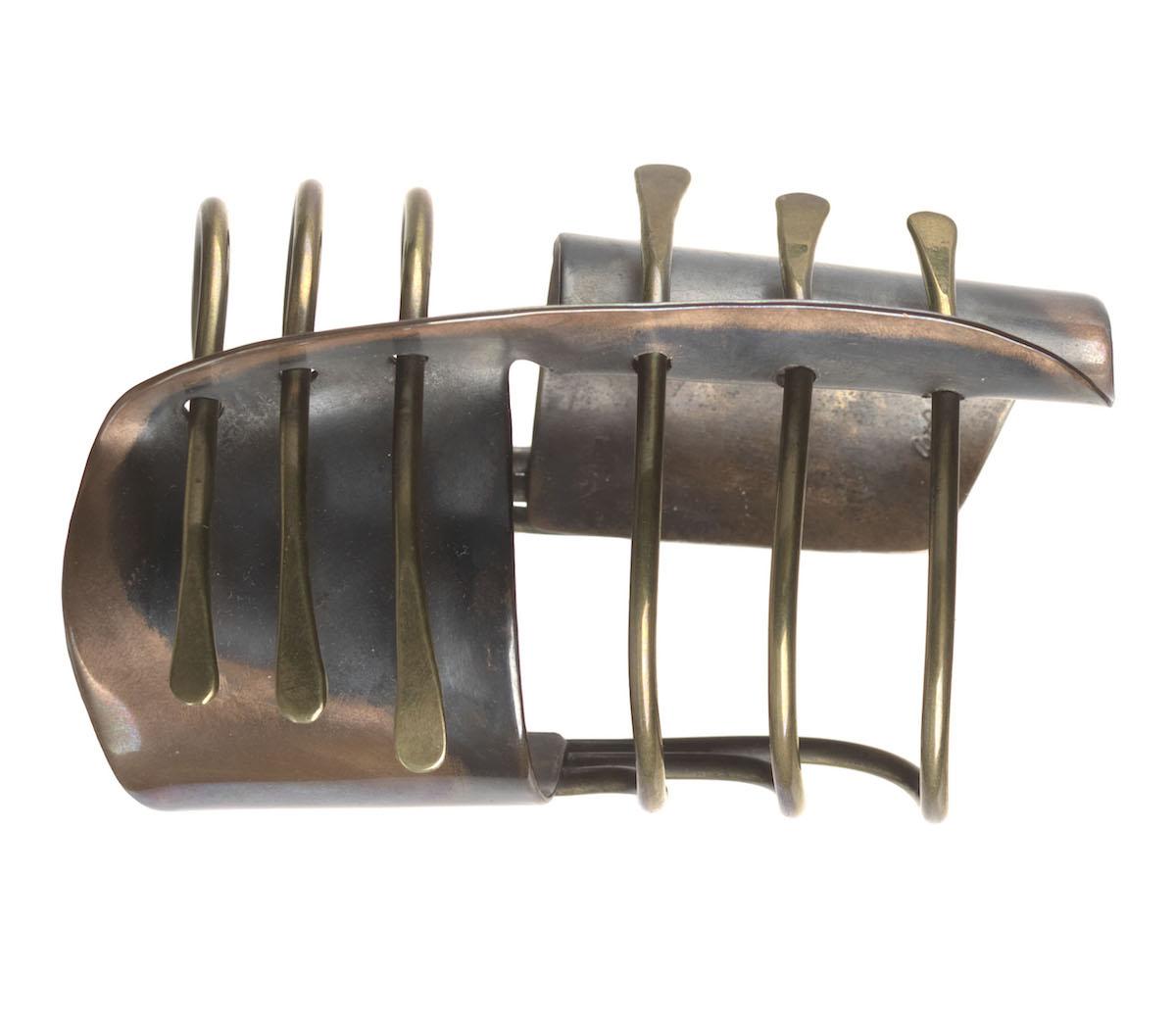 Photograph of a cuff bracelet with two curved metal surfaces, perforated by six thin lines
