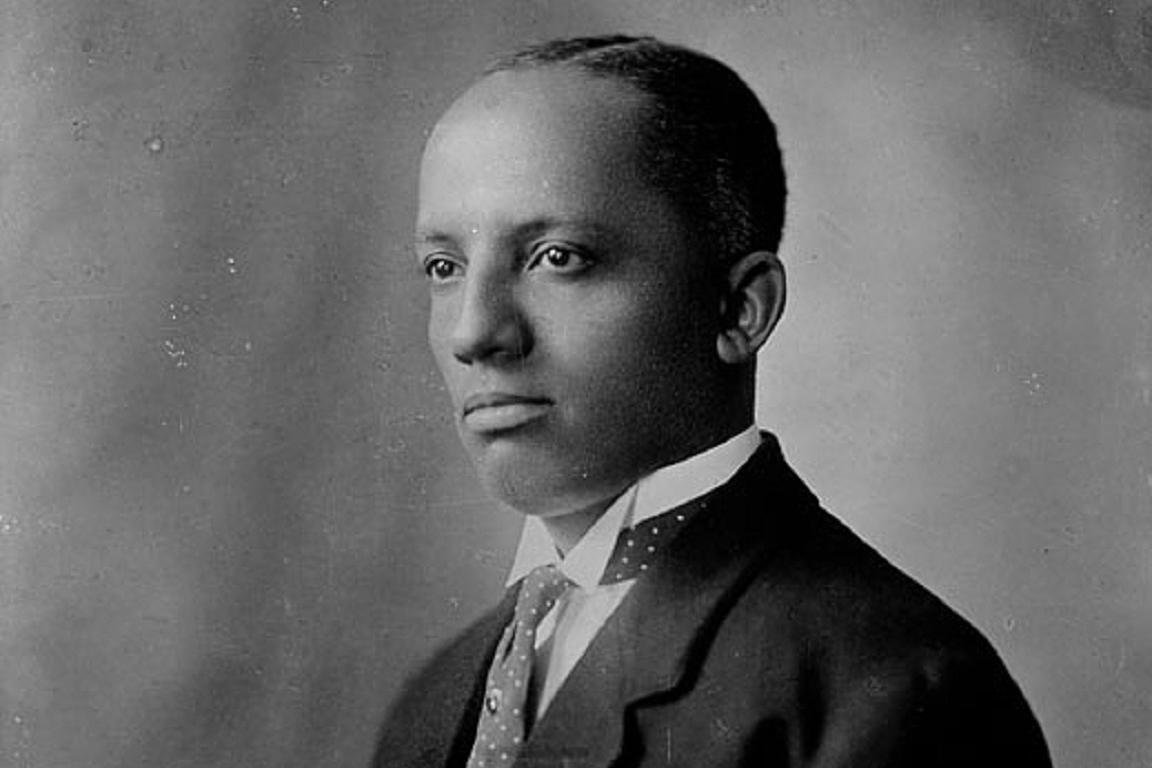 Black & white portrait photo of a younger Carter Woodson wearing a suit.