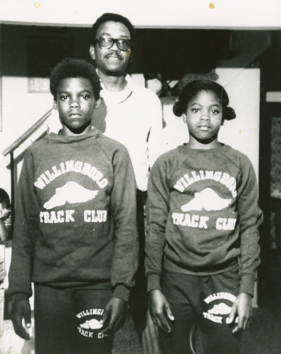 an image of Carl Lewis and hist sister standing in front of their father. 