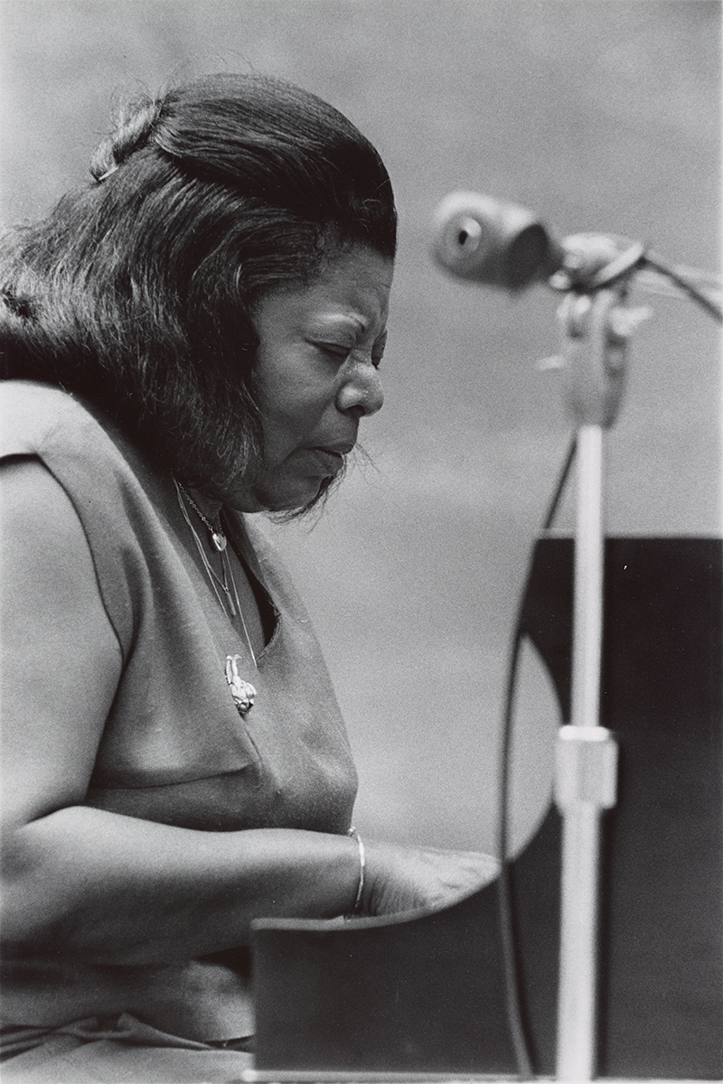 A photograph of a woman playing the piano with a microphone in the foreground.