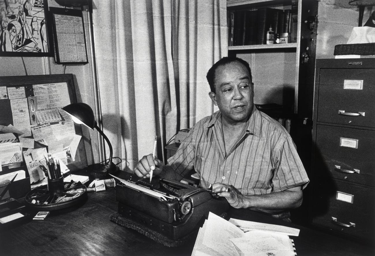 Langston Hughes sitting at a desk in front of a typewriter.