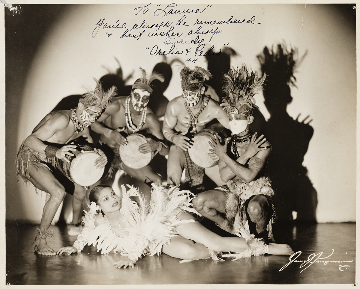 A silver gelatin print depicting a black-and-white image Princess Orelia and four (4) men in costumes with conga drums.