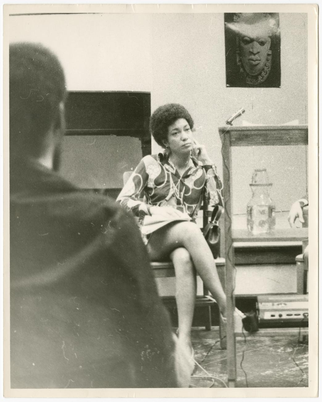 A photograph of June Jordan sitting with her legs crossed.