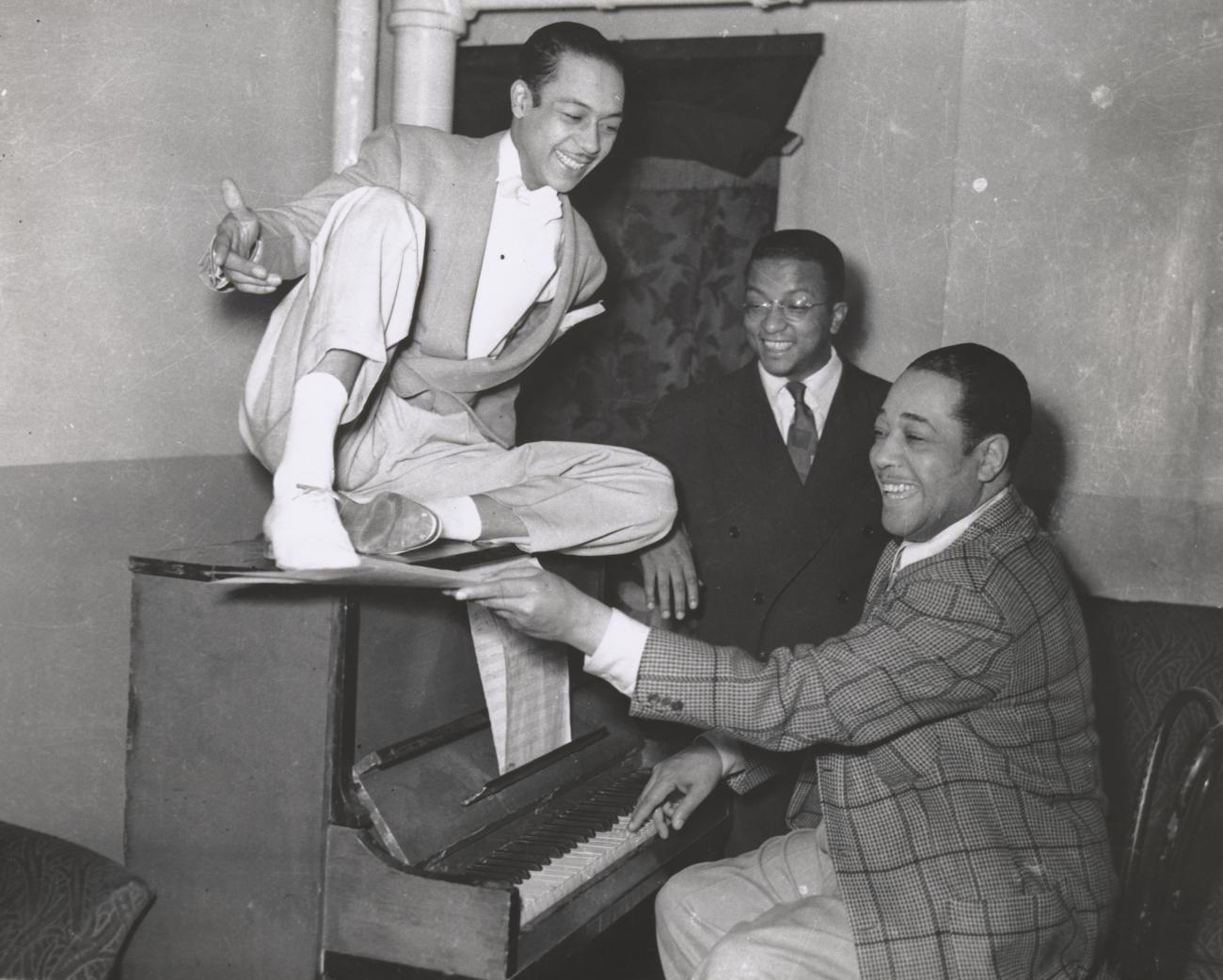 A black and white photograph of Duke Ellington with composer Billy Strayhorn and dancer Alfredo Gustar inside the Stanley Theatre in Pittsburgh, Pennsylvania.