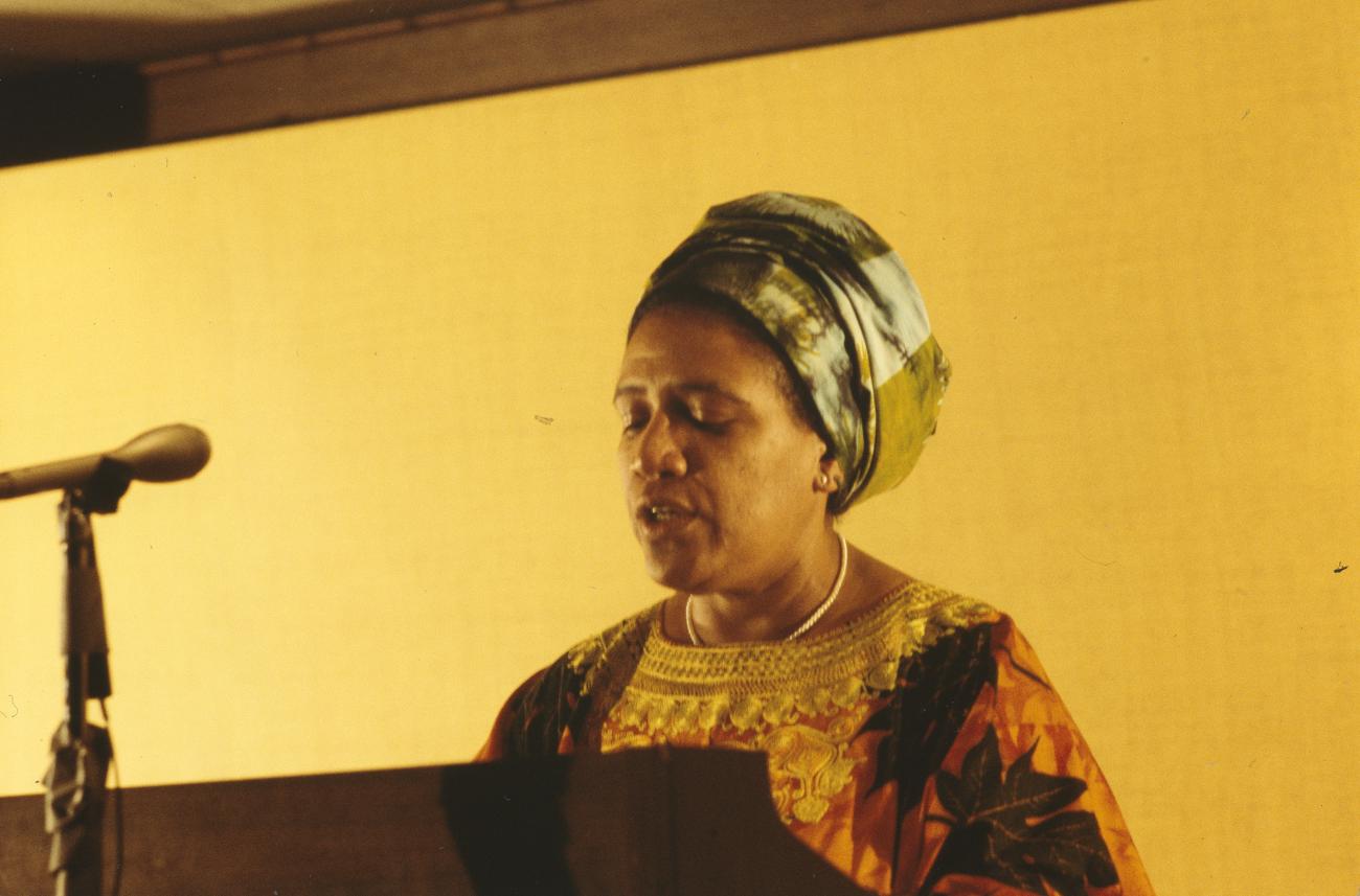 A color photograph of Audre Lorde speaking at a podium. 