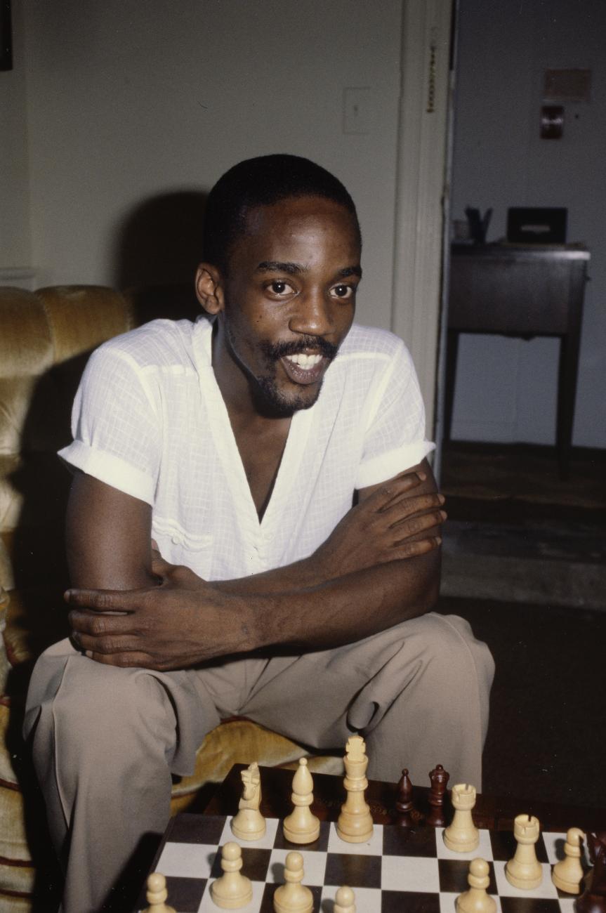 A color photographic slide featuring poet Essex Hemphill sitting in front of a chess board.