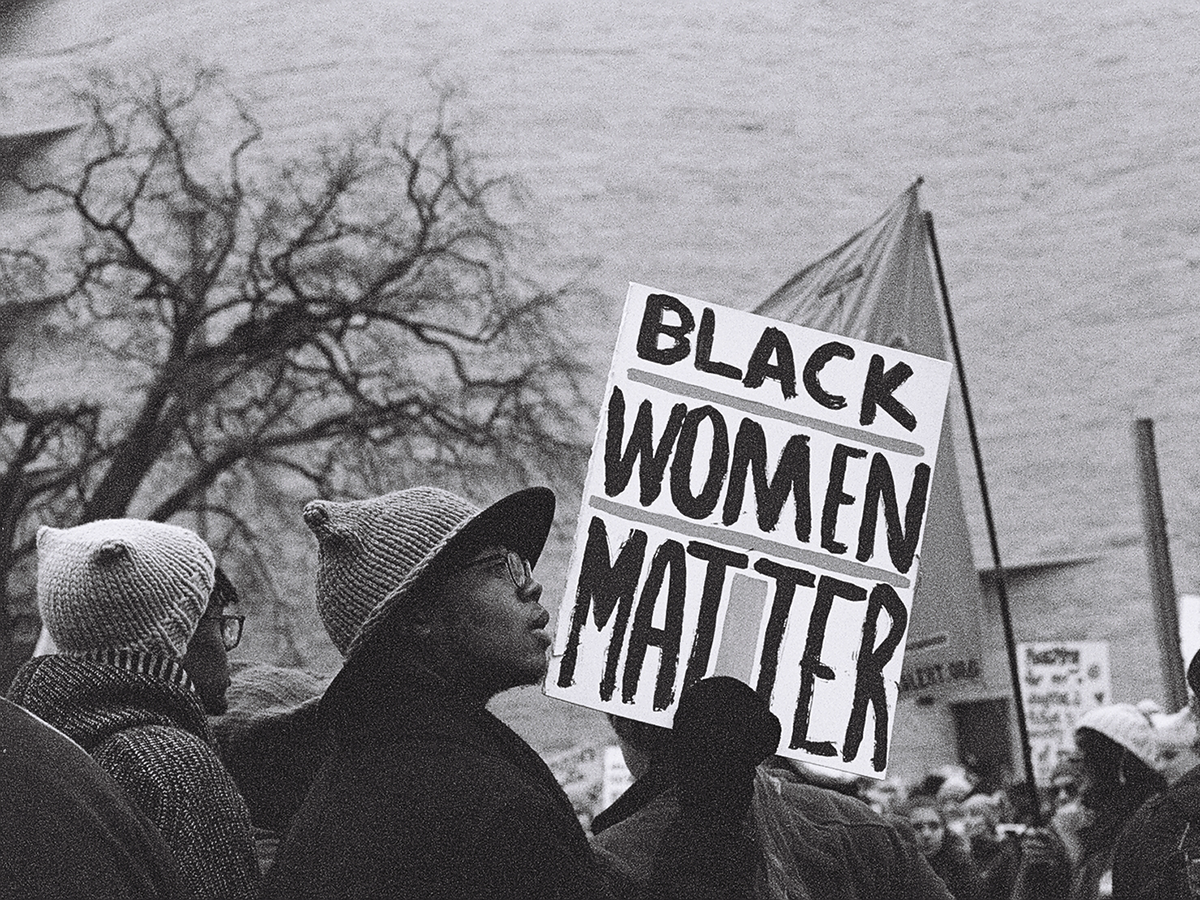 Photograph of a woman holding a sign that reads "Black Women Matter."