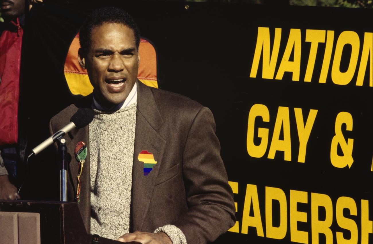 A color photographic slide of activist Phil Wilson standing in front of a podium, speaking into a microphone.