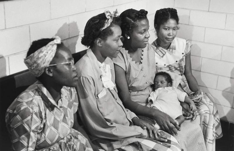 A black and white photo of four women sitting with a newborn baby.