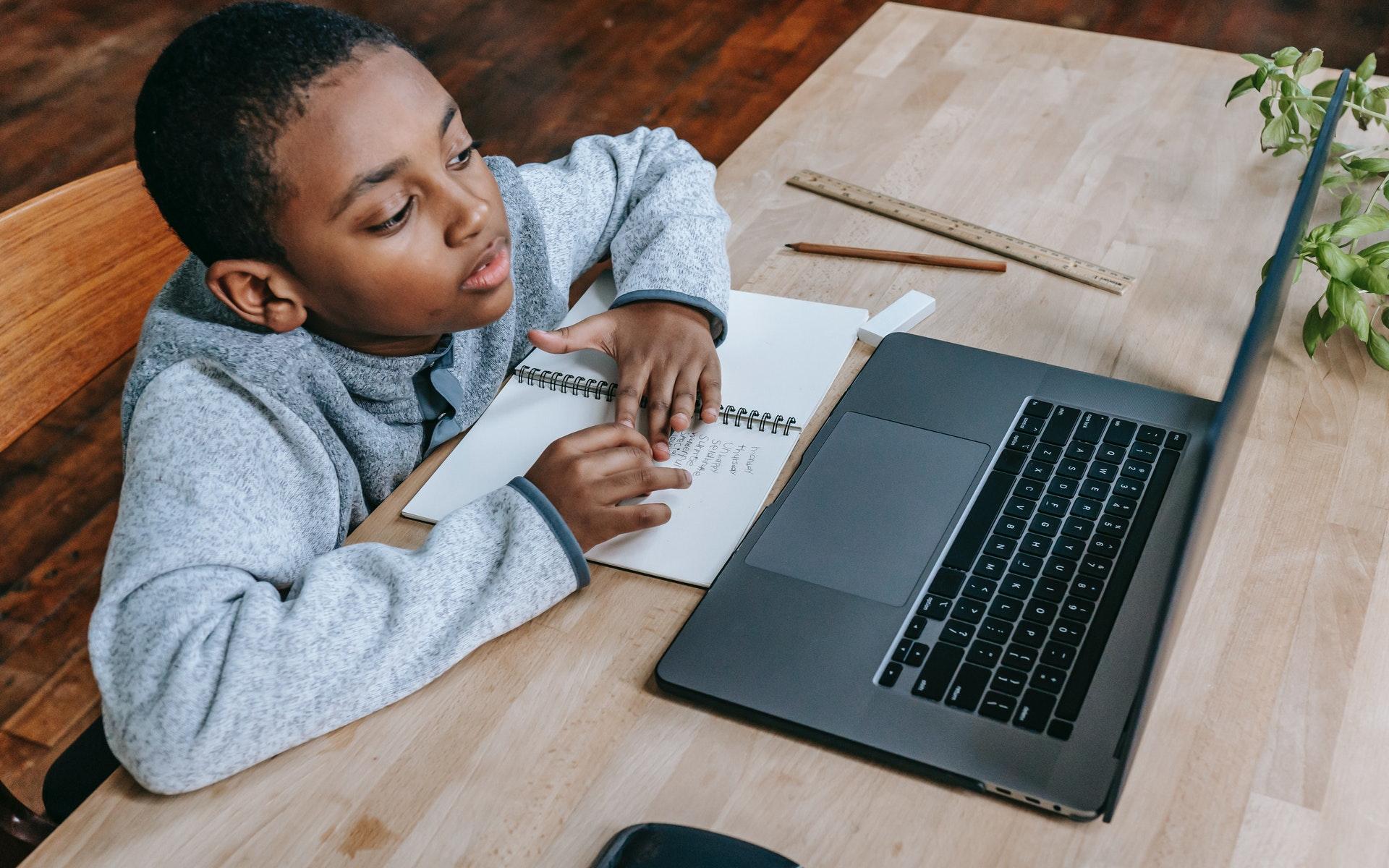 young African American boy sitting at a desk in front of a laptop computer