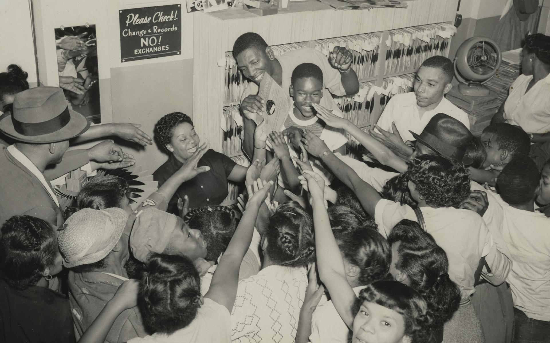 Photograph of Dinah Washington signing autographs with a crowd of people around her.
