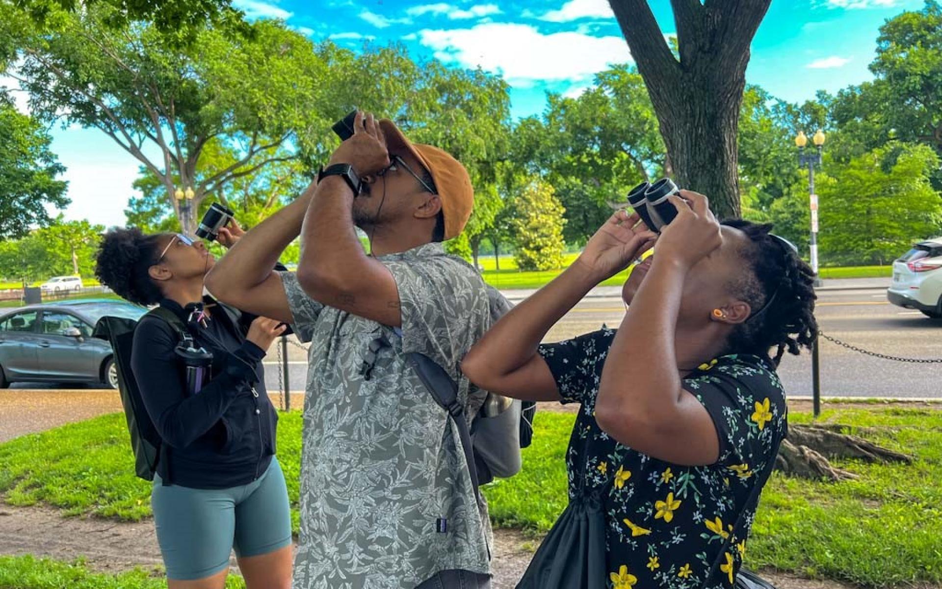 Image of an African American man and African American women using binoculars to find birds in trees