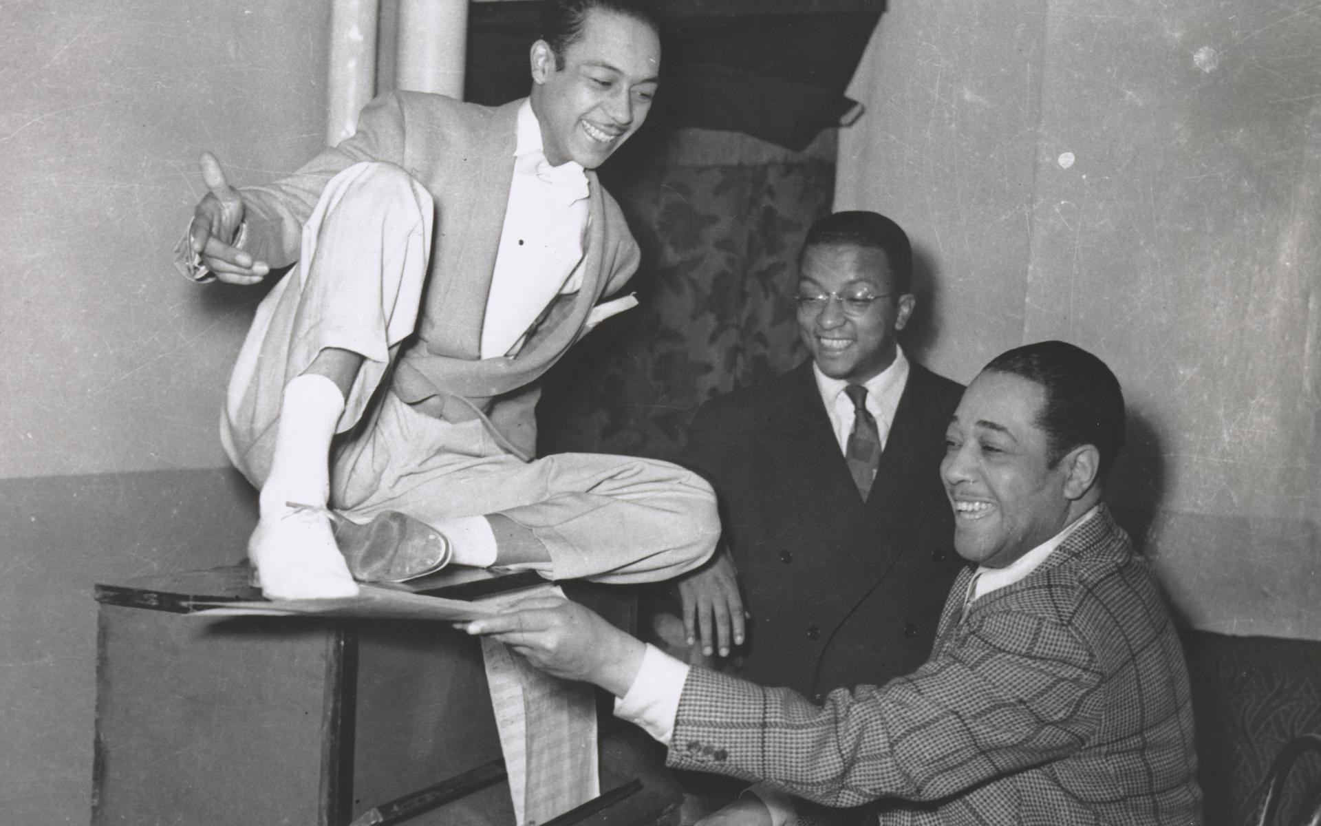 A black and white photograph of Duke Ellington with composer Billy Strayhorn and dancer Alfredo Gustar inside the Stanley Theatre in Pittsburgh, Pennsylvania.