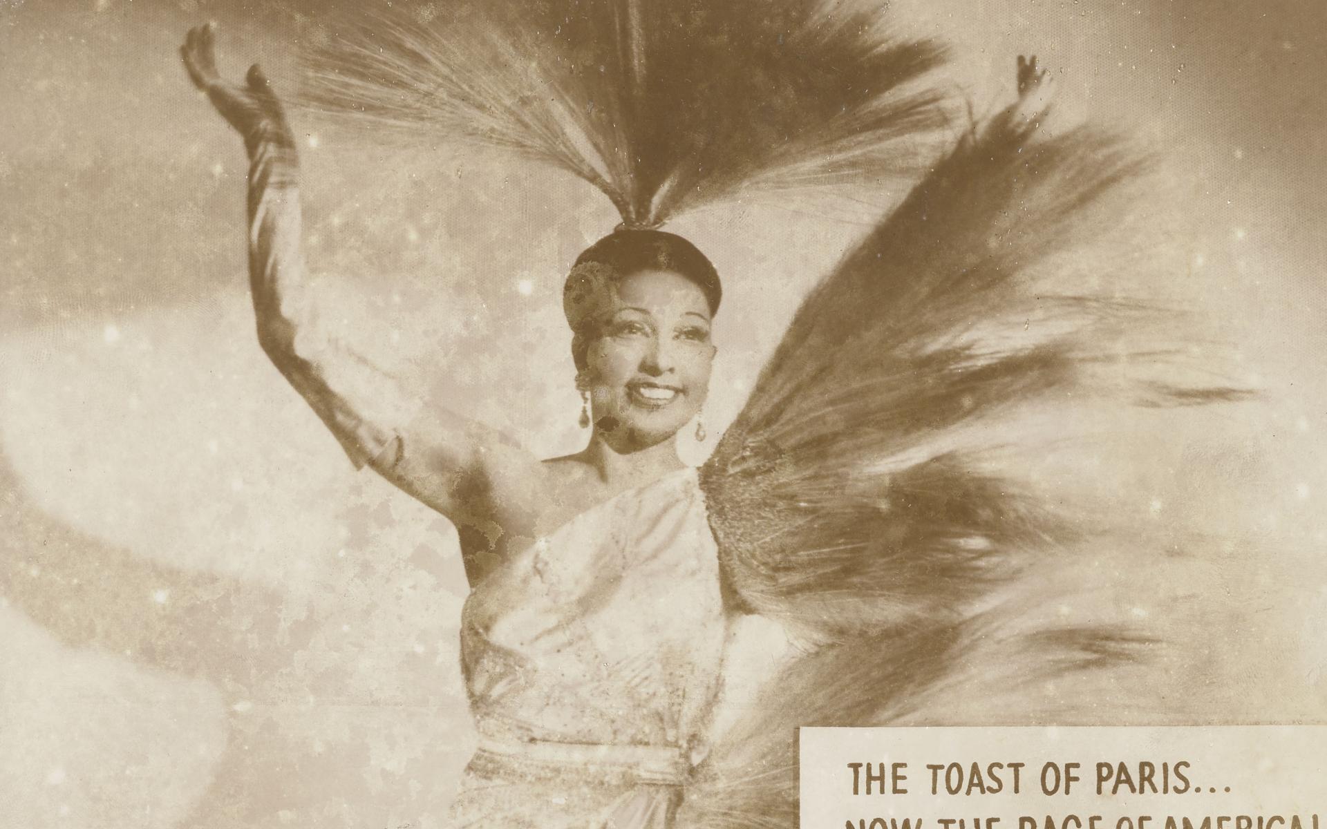 Josephine baker in costume with her hand in the air.