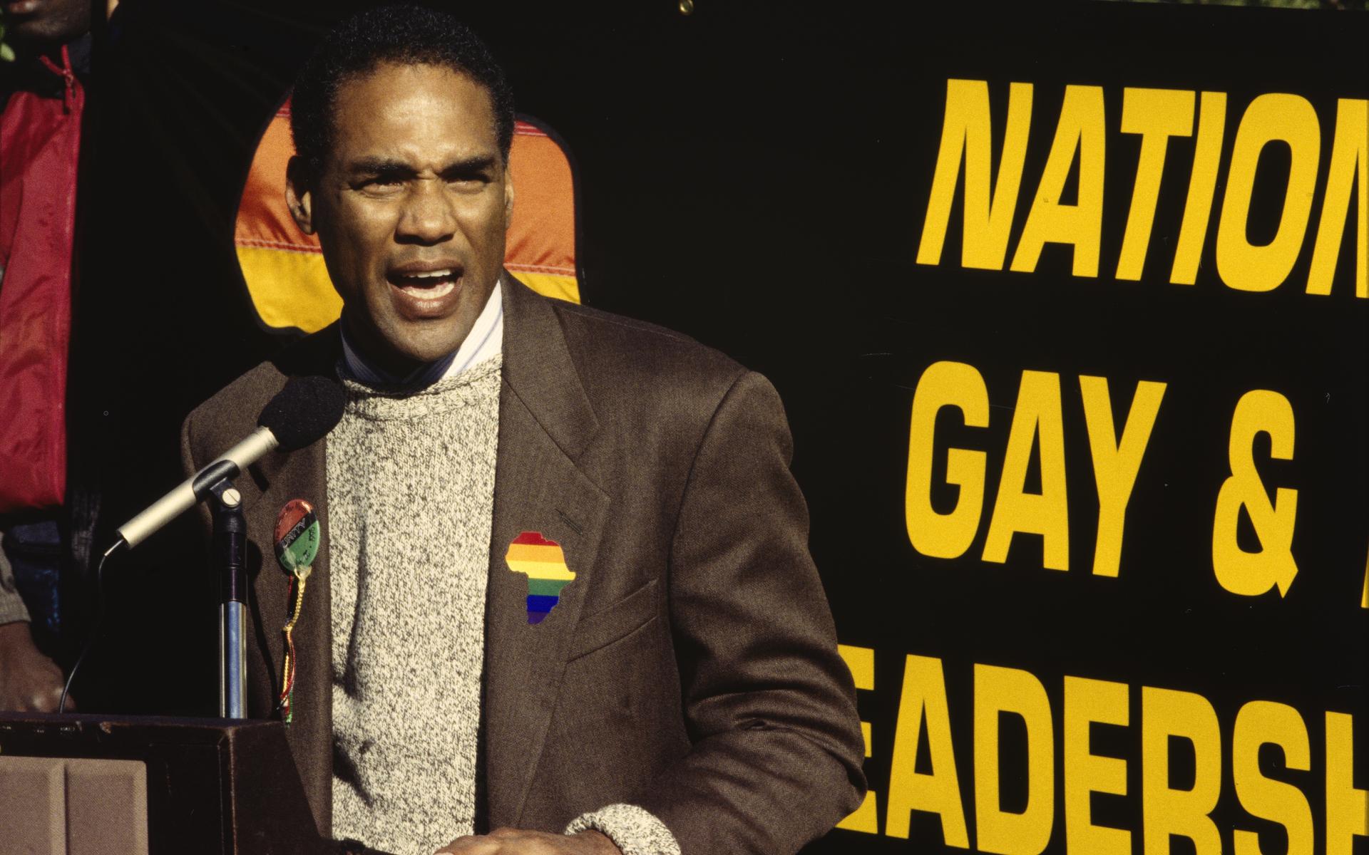 A color photographic slide of activist Phil Wilson standing in front of a podium, speaking into a microphone.