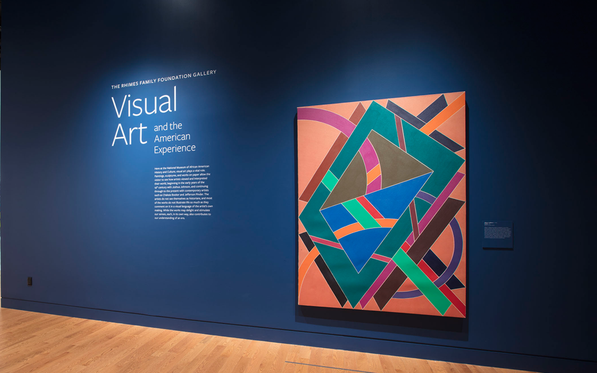Entrance to Visual Art exhibition with a colorful painting on a dark blue wall.